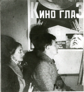 Vertov and Svilova sitting beside the poster for their film "Kinoglaz"